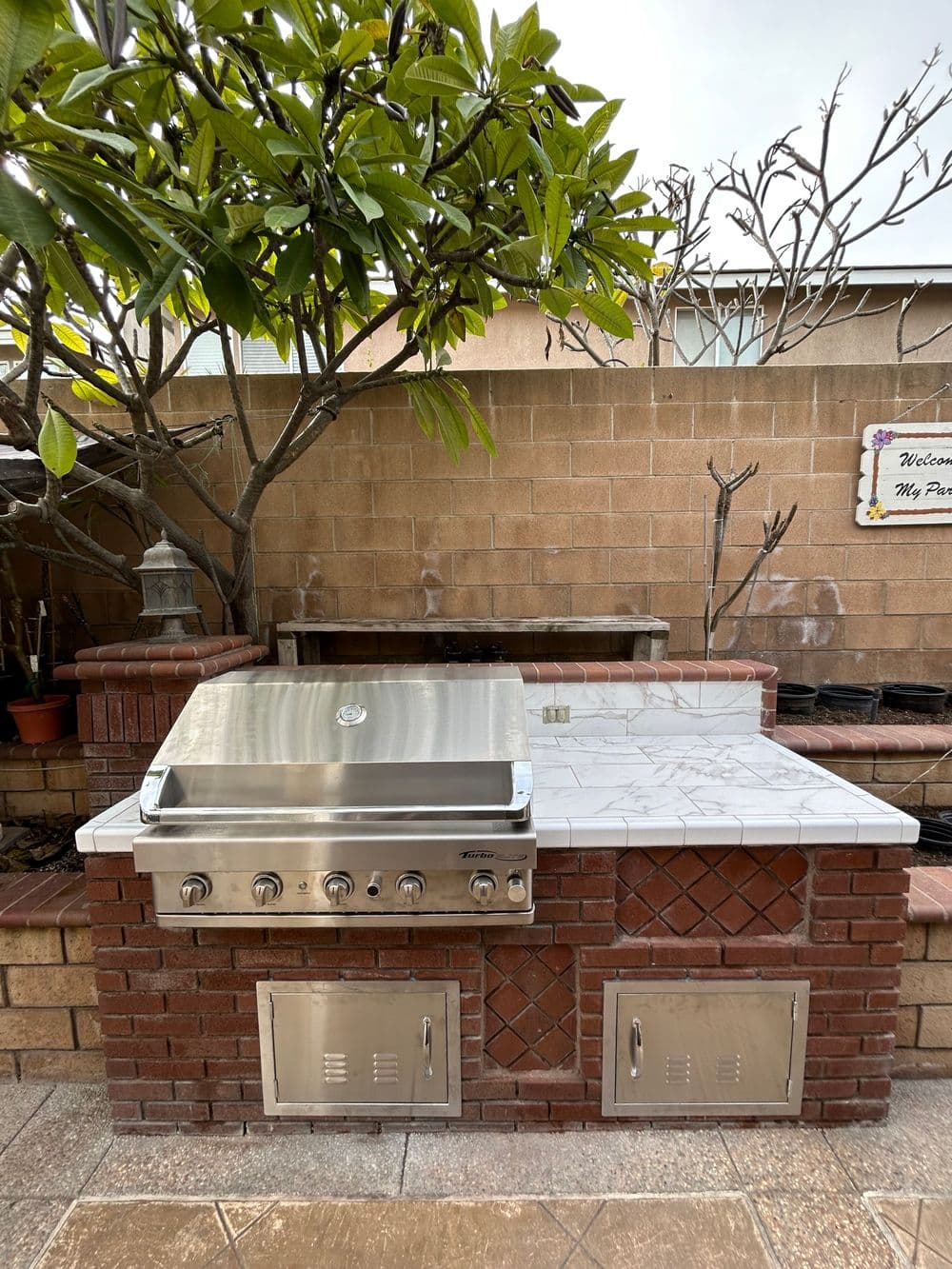 Stainless steel outdoor grill with stone countertop in a garden setting.
