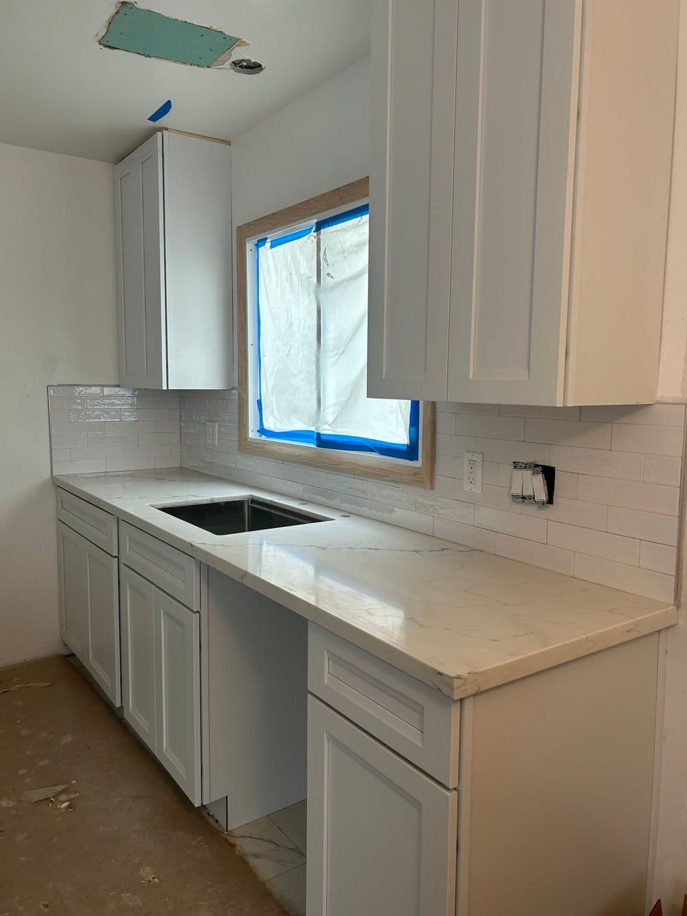 Modern kitchen with white cabinets, sleek countertop, and tiled backsplash under renovation.