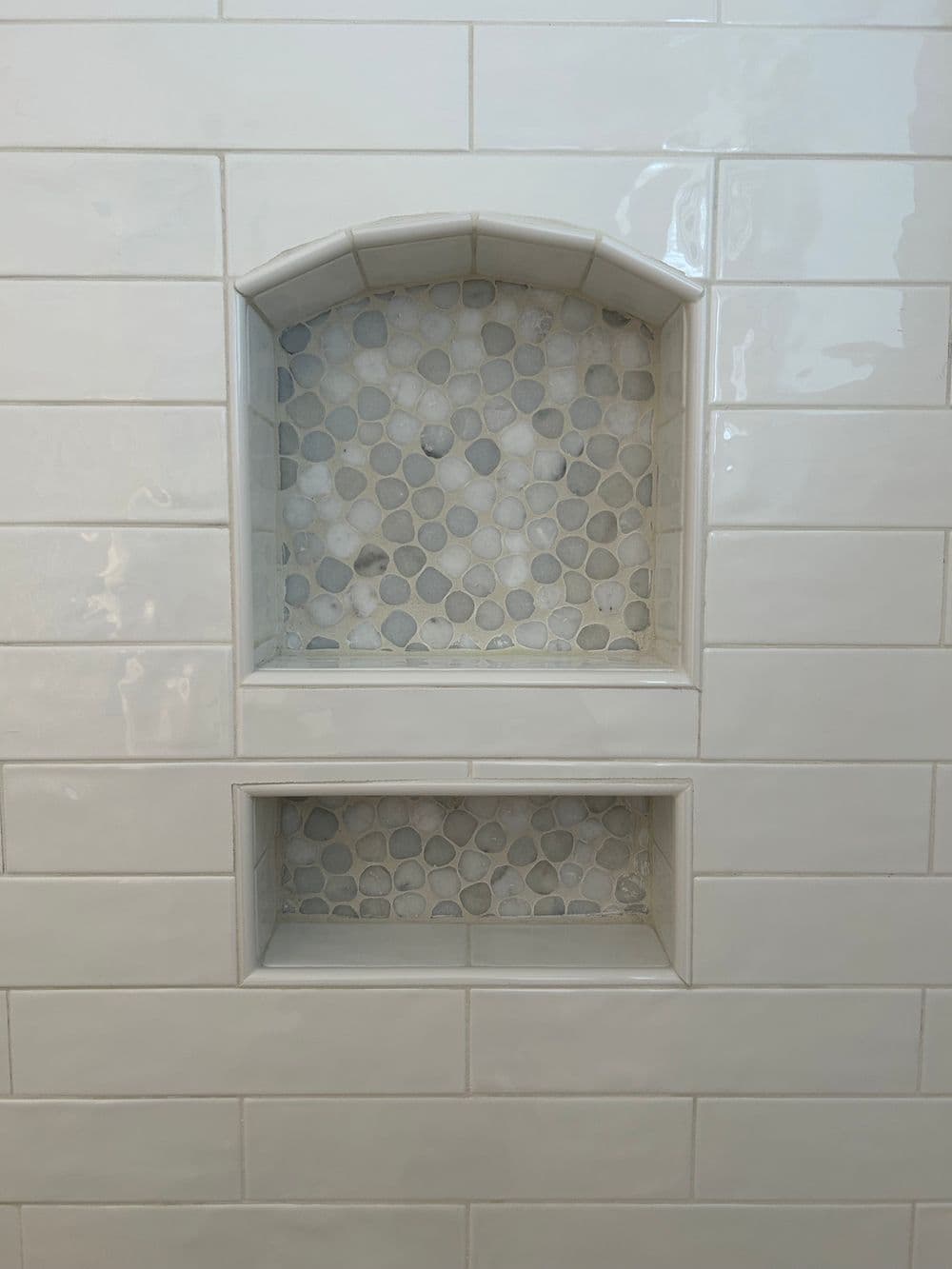 Decorative shower niches with pebble tile accents in a white tile wall.