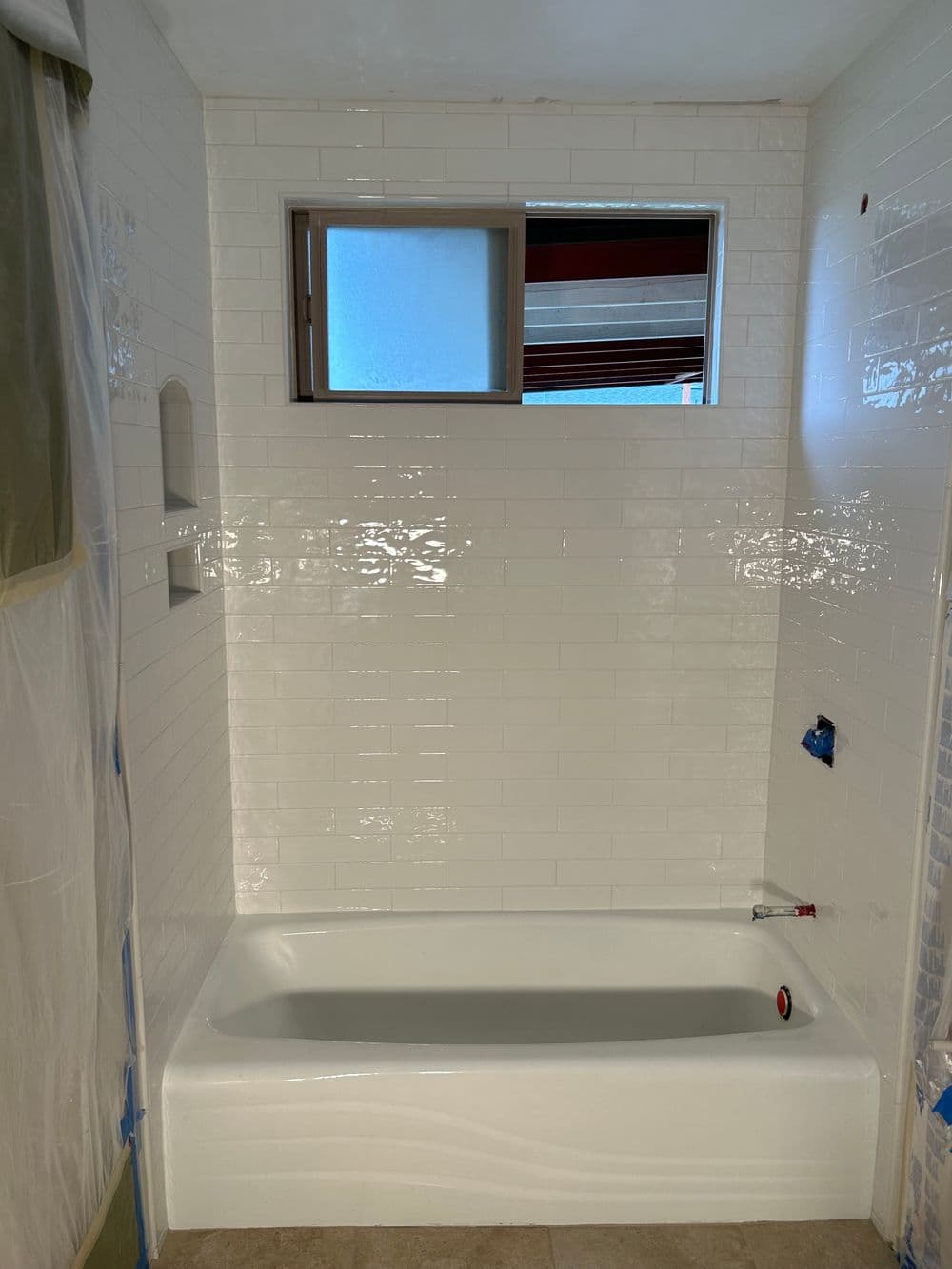 Renovated bathroom featuring a white tiled tub and window with natural light.
