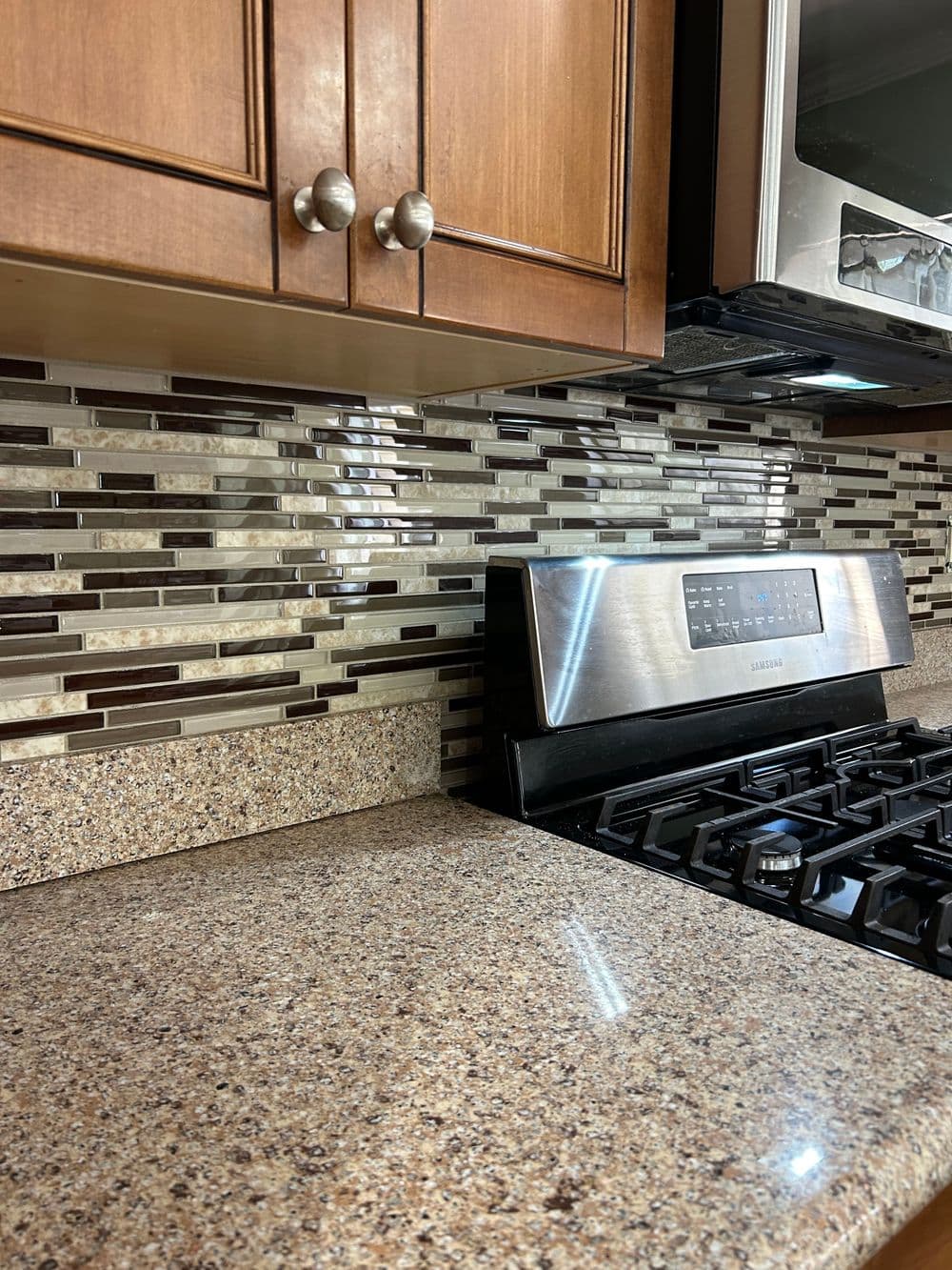 Modern kitchen with glass tile backsplash, granite countertop, and stainless steel stove.